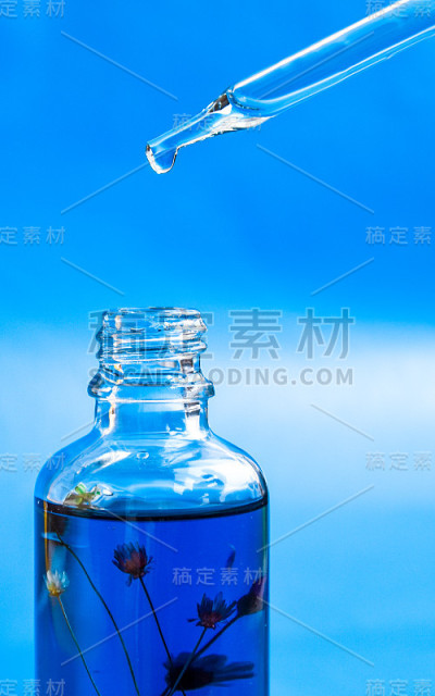 滴管玻璃瓶模型。油性液滴从化妆品吸管上落在蓝色背景上。年度颜色，