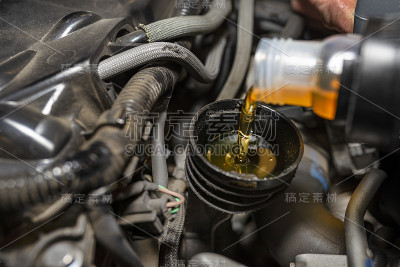 在汽车车间里，汽车修理工把新的汽车油从塑料油箱里倒进发动机里。