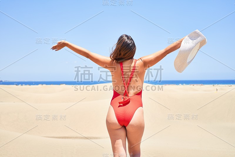 年轻美丽的女人日光浴与开放的双臂穿着夏天的swinsuit在maspalomas沙丘bech