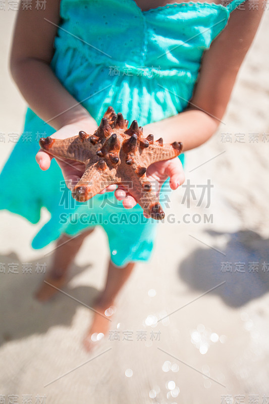 热带海滩上，可爱的小女孩手里拿着海星