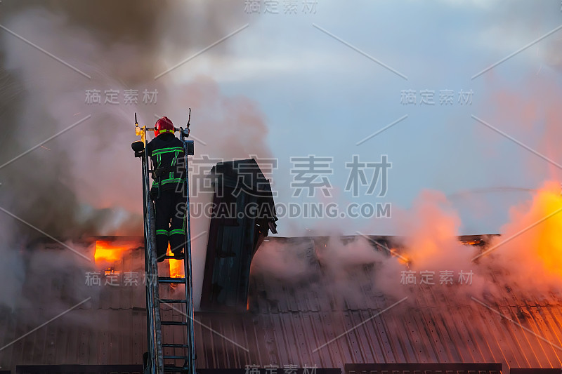 消防队员或消防队员在梯子上用烟扑灭公寓屋顶上燃烧的火焰