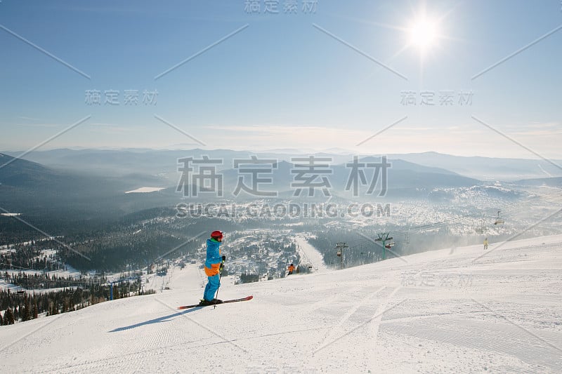 滑雪者戴着头盔站在雪山顶上，阳光灿烂，景色优美