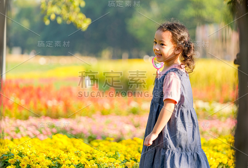 亚洲小女孩拿着粉红色的放大镜转身微笑着站在晨曦中的花园前