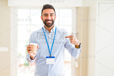 英俊的西班牙男子戴着身份证和喝咖啡与惊讶的脸指向自己的手指