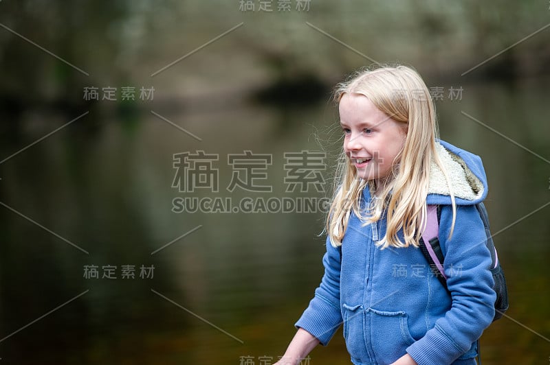 微笑年轻的金发女孩与模糊的河流场景背景