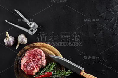 牛柳片，用刀切肉，调味料-迷迭香，胡椒，盐，大蒜。旧木板上的石头黑色桌子