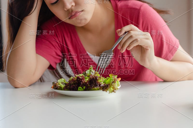 饮食。亚洲年轻漂亮的女人无聊的情绪和拒绝吃新鲜的绿色蔬菜沙拉在桌子上在家健康，营养，减肥，生活方式，