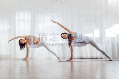 两个迷人的专注冷静的瑜伽女孩做伸展侧角瑜伽姿势。瑜伽工作室内部。