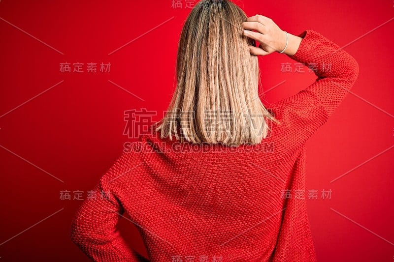 年轻美丽的金发女人穿着休闲毛衣越过红色孤立的背景向后思考怀疑与手在头上