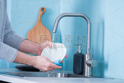 一个男人在厨房里用蓝色的生态海绵洗盘子，厨房的墙壁是蓝色的