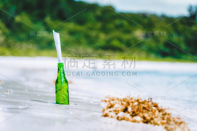 瓶子与信息在白色天堂沙滩与模糊的丛林背景概念