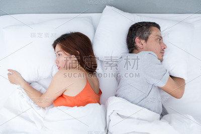 一对背靠背躺在床上的年轻夫妇