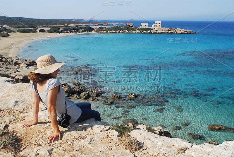 漂亮女孩坐在海滩的悬崖边