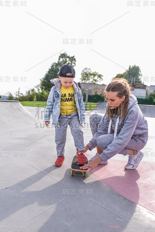 带着一个小男孩的妈妈，在滑板上训练，在运动和健身方面提供帮助和支持。关怀的养育和支持。在夏天的运动场