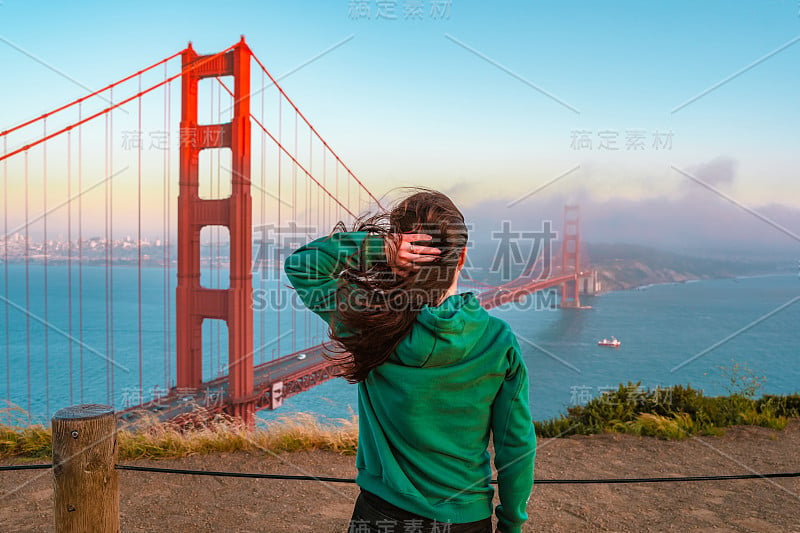 日落时分，旧金山，一位身穿绿色帽衫的年轻女子站在小山上俯瞰金门大桥