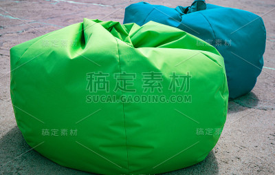两张绿色和蓝色的布袋椅放在露天的石砌路面上。有选择性的重点。适合海上度假、休闲、旅游。