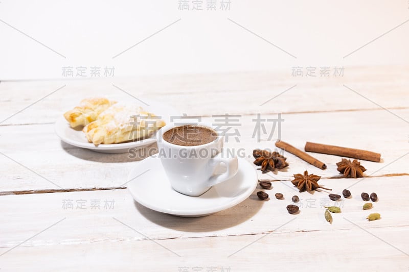 一杯咖啡配茶碟，肉桂棒，八角，羊角面包，白色的木质背景