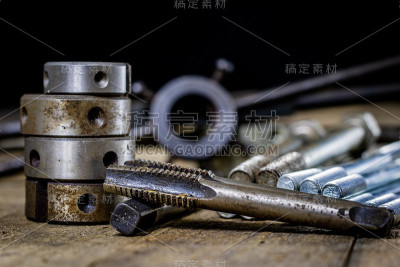 金属加工工具放在工作台上。一个旧的满是灰尘的车间里的螺纹模具和丝锥。黑色背景。