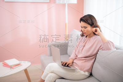 紧张的亚洲年轻人坐在沙发上使用笔记本电脑。