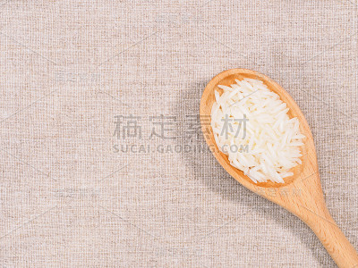 印度长粒印度香米，用木勺斜放在米色织物背景上