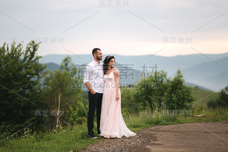 美丽的新婚夫妇站在绿油油的山坡上。新郎和新娘在喀尔巴阡山脉。男人亲吻女人的额头