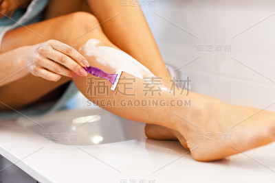 年轻女子早上在浴室里刮腿毛
