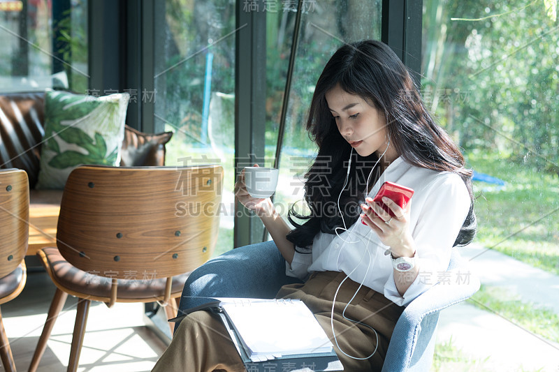 一个女人拿着智能手机在咖啡馆里听着音乐。女商人在笔记本上读笔记。年轻的女企业家拿着咖啡杯。休闲，生活