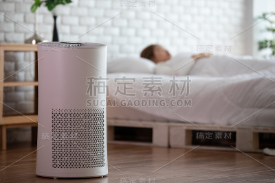 女人睡觉用空气净化器在舒适的白色床室过滤和清洁去除灰尘PM2.5 HEPA在家里，为新鲜空气和健康的