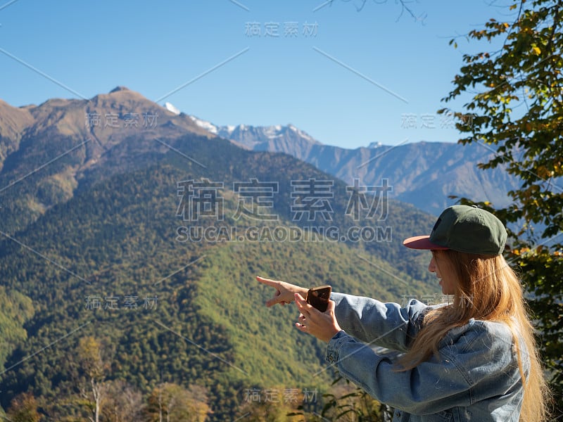 长发女孩手里拿着手机，手指着山峰