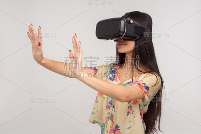 年轻漂亮的女人戴着VR眼镜，举着手掌，正面冷静的表情，站着玩电子游戏