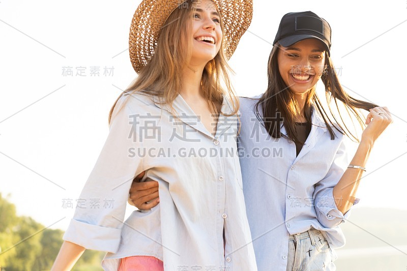 两个年轻漂亮的女人在海滩上散步。夏日里，女性朋友们在海滩上散步，开怀大笑。