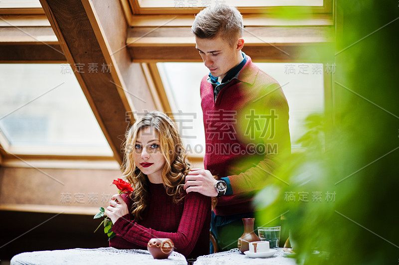 年轻漂亮时髦的夫妇穿着红色的裙子在一个复古的咖啡馆，有大窗户的屋顶