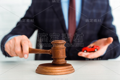 抱着木槌的拍卖师和模型的汽车的裁剪视图