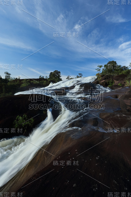 热带雨林中的瀑布景观，缓慢的快门速度使水变得模糊。蓝色的天空背景,泰国