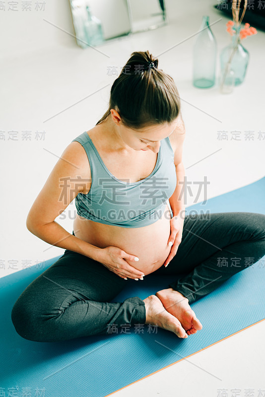 一个年轻漂亮的怀孕女孩穿着运动服在做瑜伽，在工作室的垫子上做体式小体式