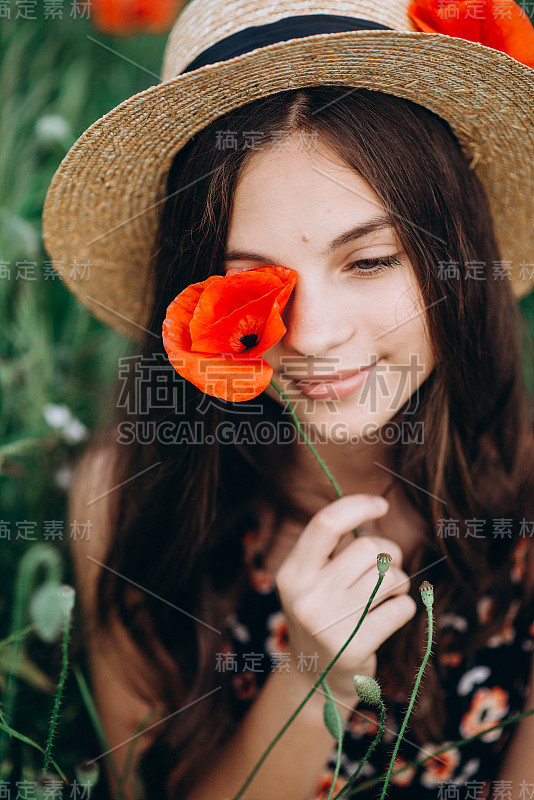 美丽的年轻女孩戴着一顶帽子在草地上闭上一只眼睛与红色的罂粟花。一个女孩的特写。