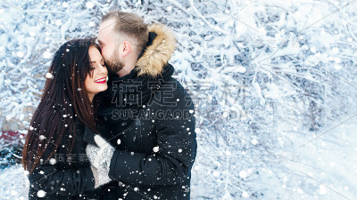 快乐的年轻夫妇在冬天的雪公园拥抱。家庭在户外。