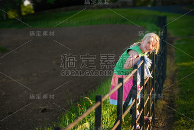 漂亮的金发女孩在夕阳下爬篱笆