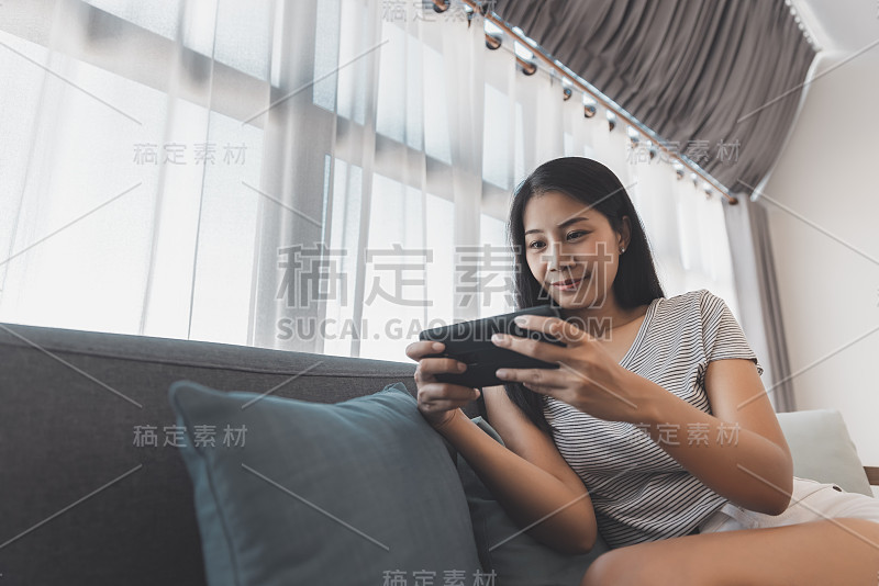 亚洲妇女放松和使用手机在客厅的沙发在家里