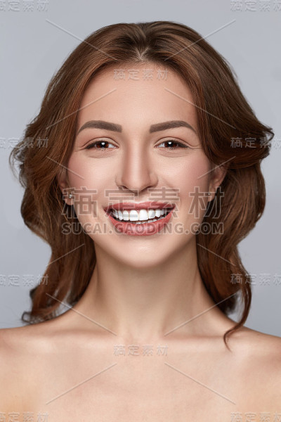 美丽微笑的女孩，干净的皮肤，自然的化妆，和白色的牙齿在灰色的背景