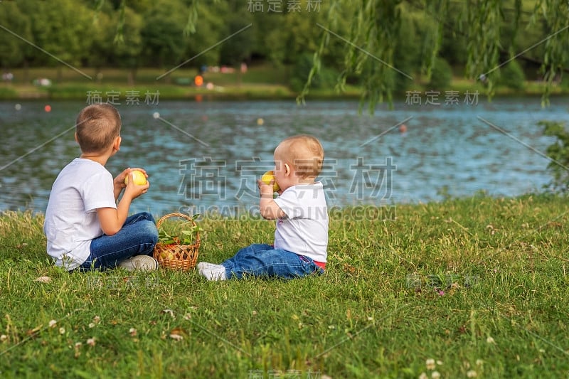 孩子们，一个男孩和一个女孩带着野餐篮和苹果坐在湖边。