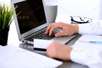 商业妇女的手使用信用卡和笔记本电脑的特写
