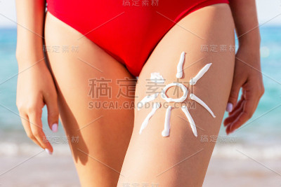 在海滩上晒太阳的女人用防晒霜在她的腿上画太阳