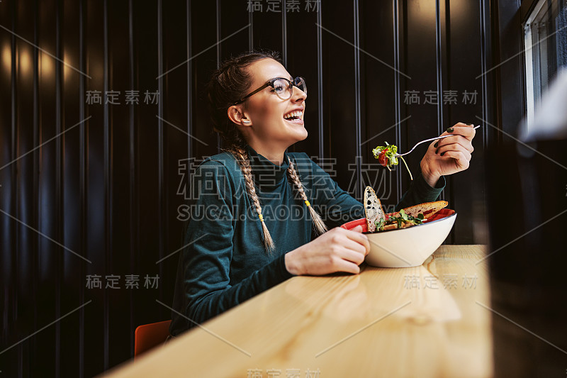 年轻的女孩坐在餐馆靠窗的地方，午餐吃沙拉。健康的生活方式的概念。