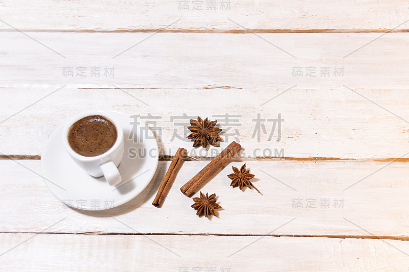 一杯咖啡和茶托，肉桂棒，八角在白色的木头背景