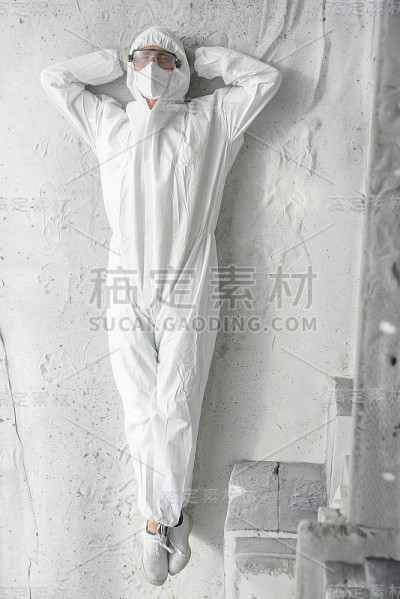 一名男子身穿白色防护服，戴着呼吸器和塑料透明眼镜。