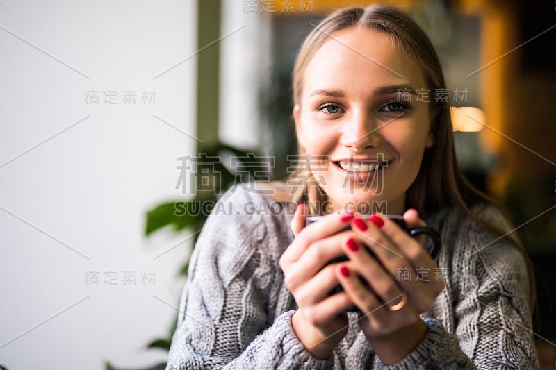 美丽微笑的女人在咖啡馆喝咖啡。一个成熟女人在自助餐厅喝着热卡布奇诺看着镜头的肖像。喝咖啡的漂亮女人。