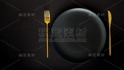 黑色的空陶瓷盘子与金色的餐具(刀叉)在黑色的背景(桌子)。