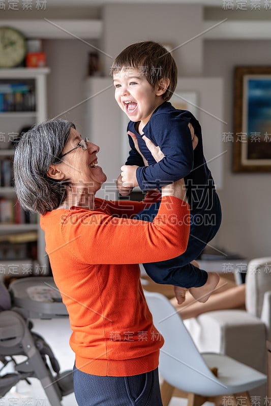 快乐的奶奶和她的小孙子玩在她的怀里在空中。保姆。家里的生活方式。不同年龄的家庭纽带。