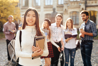 一个亚洲女孩站在大学的院子里，手里拿着书。